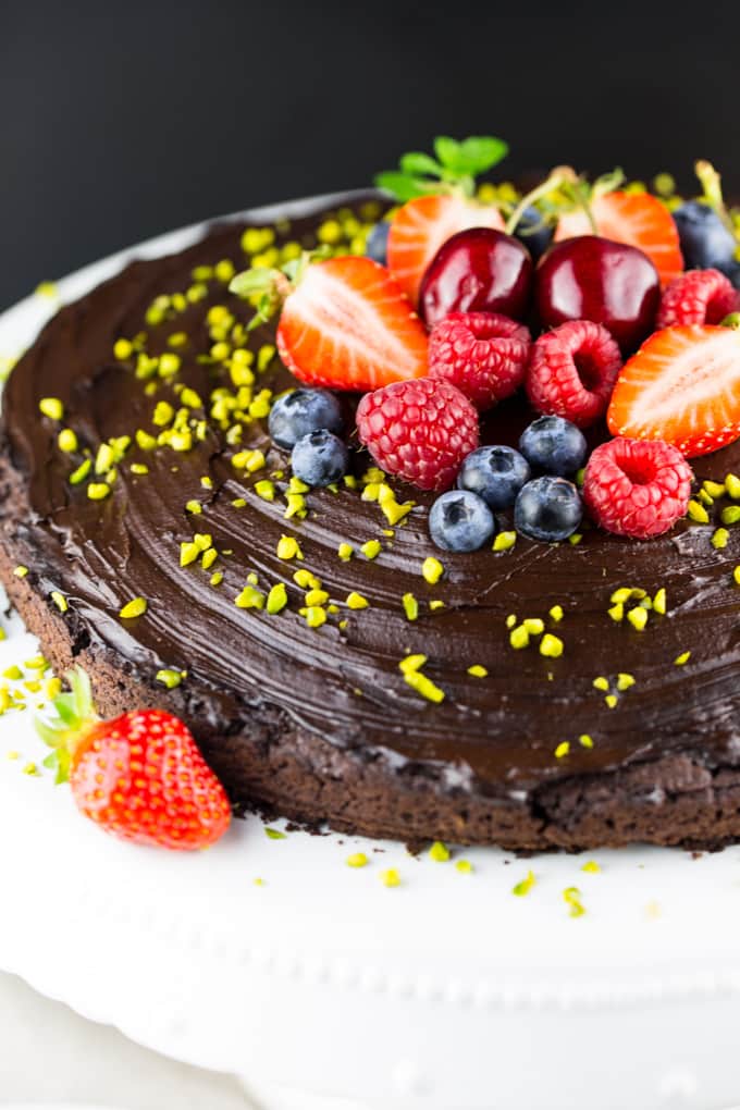 a close-up photo of a vegan chocolate cake topped with berries on a cake plate