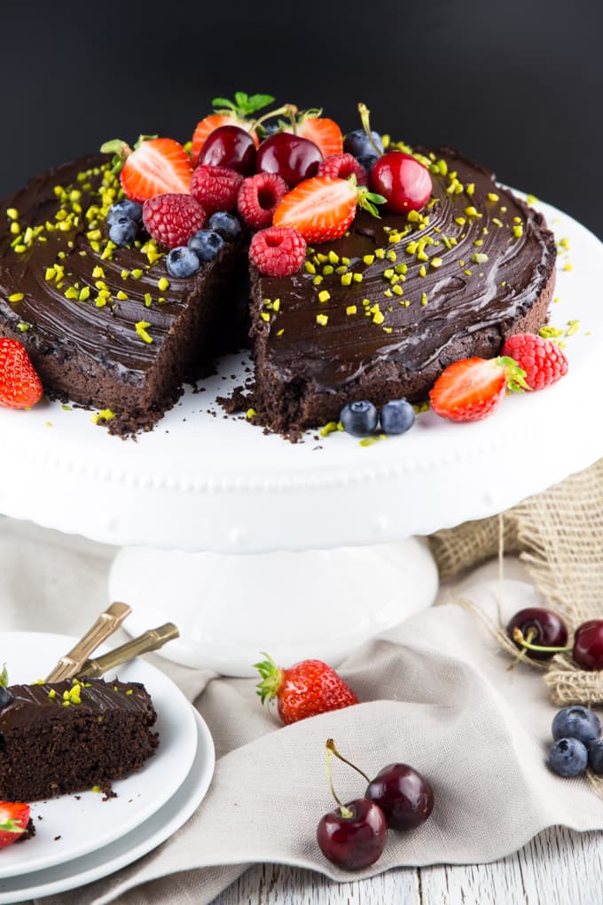 a chocolate cake with chocolate frosting on a cake platter with two plates and forks on the side