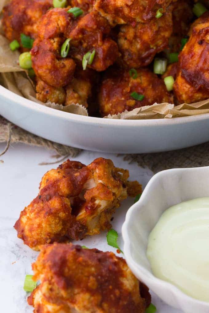 cauliflower wings on a marble counter top with a small bowl of vegan aioli on the side