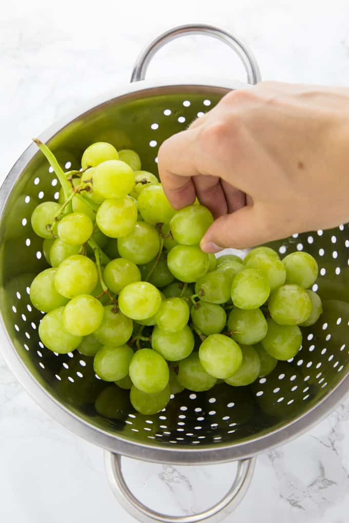 a hand picking white grapes in a silver collander on a marble counter top