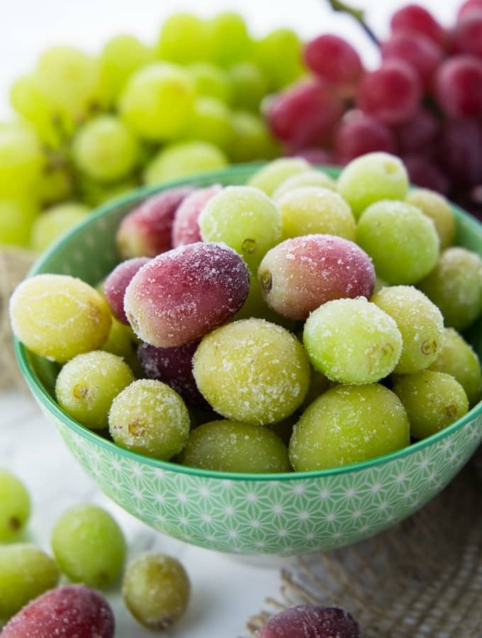 a bowl of frozen grapes on a marble counter top with fresh grapes in the background 