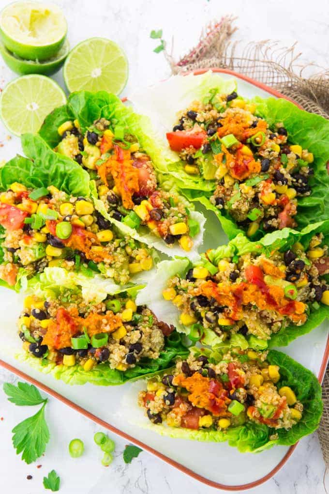 Vegetarian Lettuce Wraps on a white plate on a marble counter top with lime halves and roughly chopped parsley in the background 