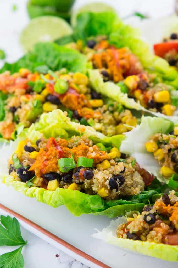 close-up of four vegetarian lettuce wraps with quinoa and black beans on a white plate with lime halves in the background 