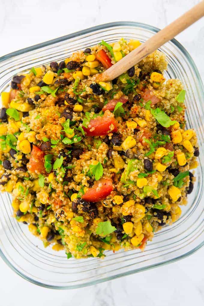 quinoa, black bean, corn salad in a glass bowl with a wooden spoon on a marble counter top 