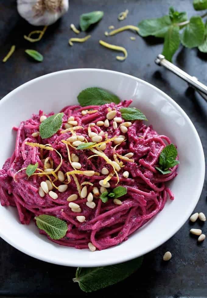 A white bowl with beet pasta on a black counter top