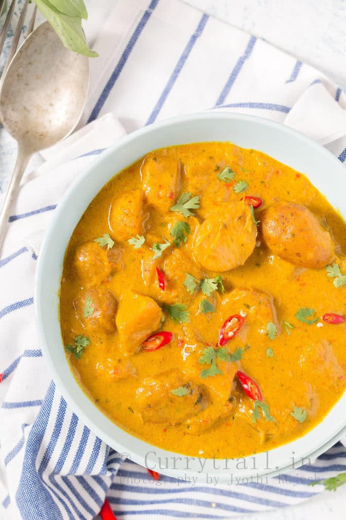 vegan pumpkin curry in a white bowl on a white and blue napkin with a spoon on the side