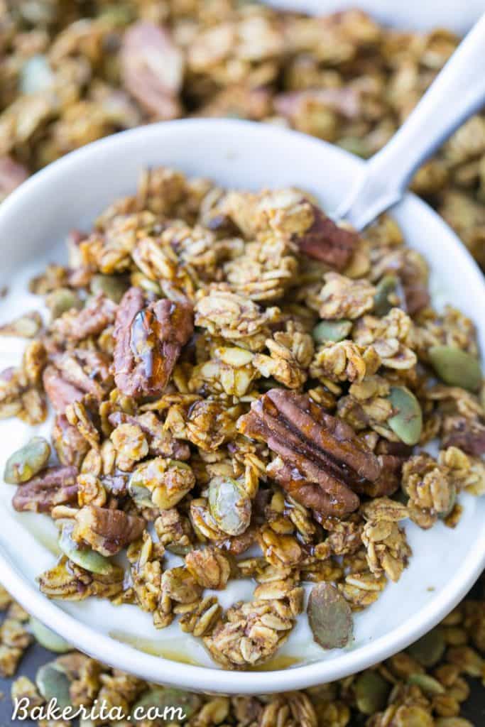 pumpkin granola in a white bowl with a spoon and more granola in the background