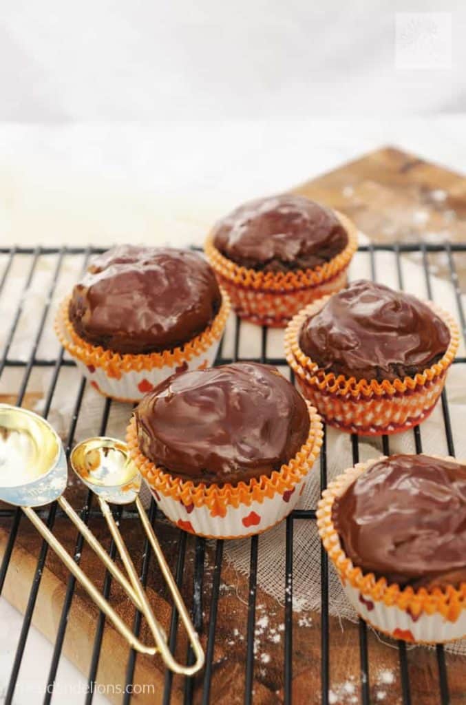 five chocolate covered pumpkin cupcakes in red and orange muffin liners on a cooling rack