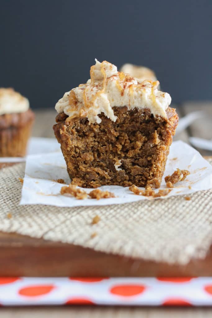 a vegan pumpkin cupcake on a white sheet of paper on a wooden board with another cupcake in the background