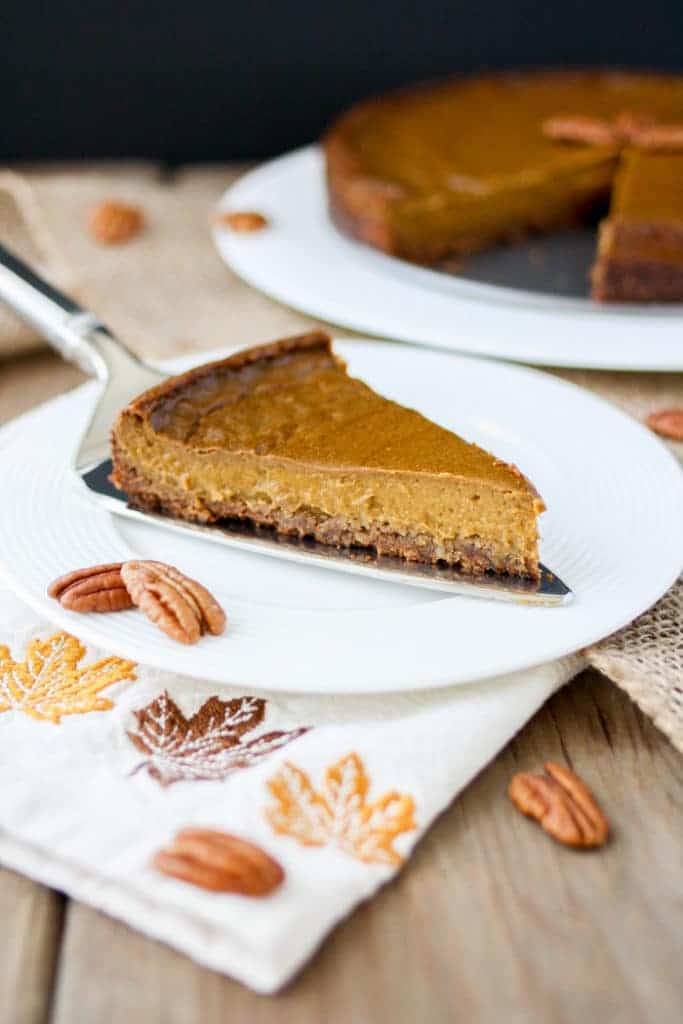 a slice of vegan pumpkin pie on a white plate with the rest of the pumpkin pie in the background