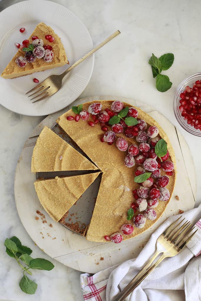 two plates of vegan pumpkin cheesecake with pomegranate seeds on a marble counter top