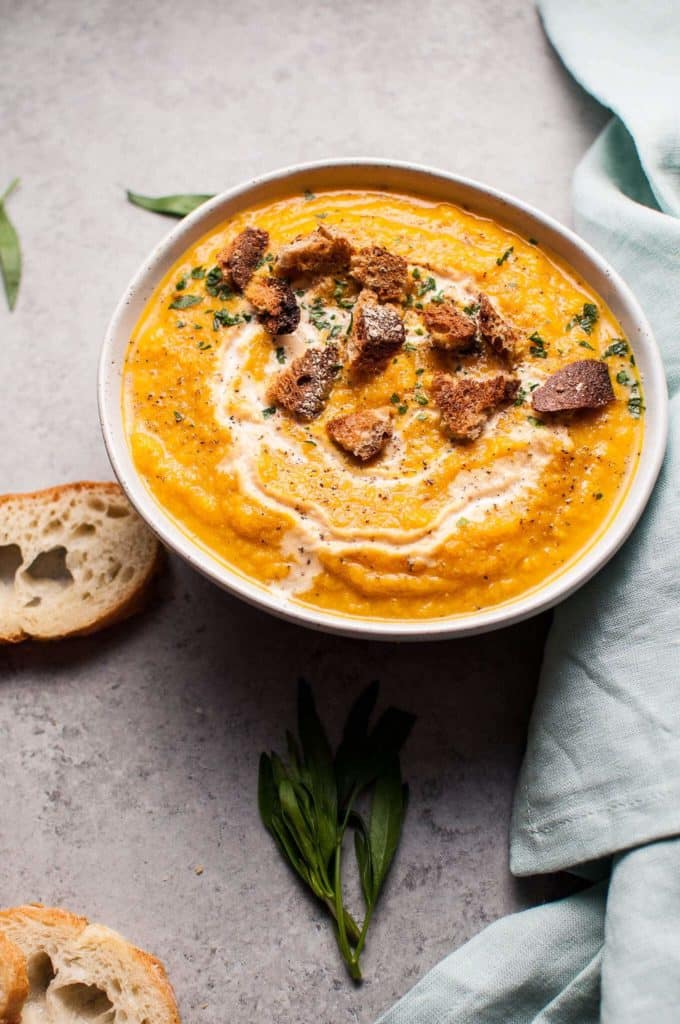 vegan pumpkin soup in a white bowl on a concrete counter top with two slices of bread on the side