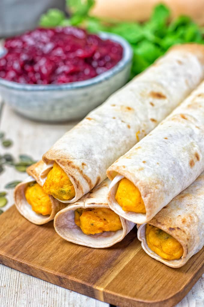 a stack of vegan pumpkin taquitos with a bowl of cranberries in the background