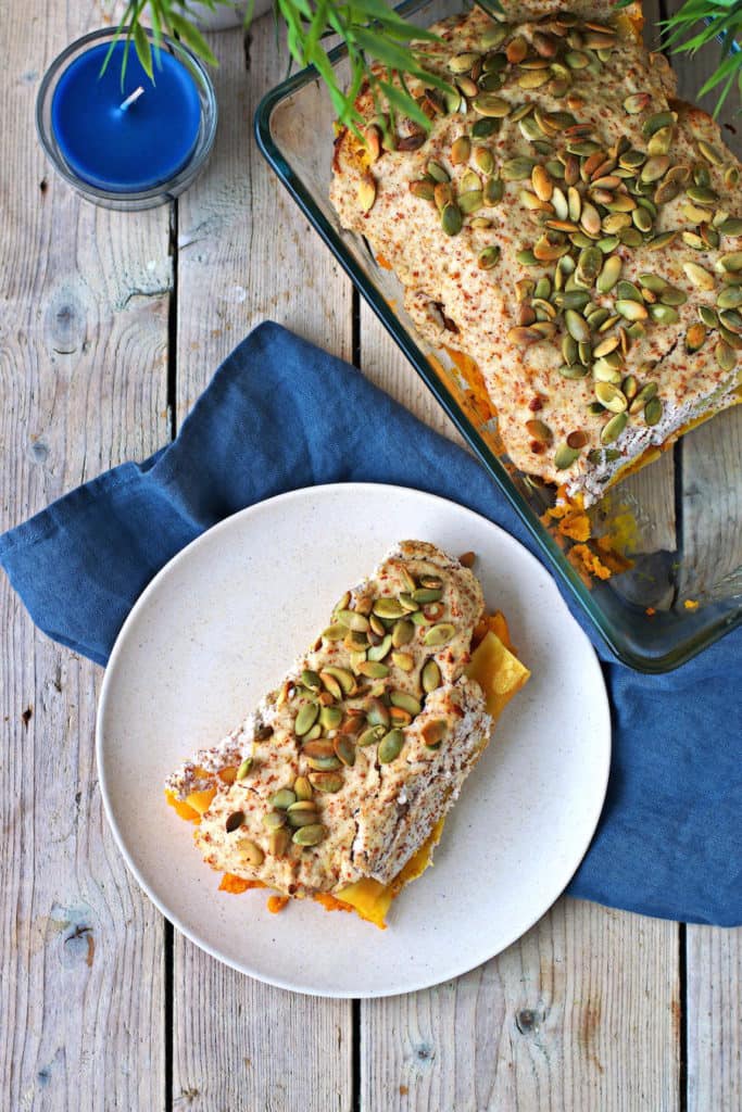 pumpkin cannelloni on a white plate with a casserole dish and a blue napkin on the side