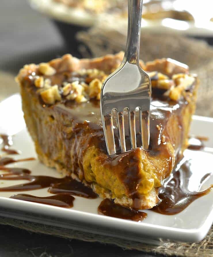 a fork piercing into a slice of vegan pumpkin pie on a white plate with caramel sauce on top and on the side