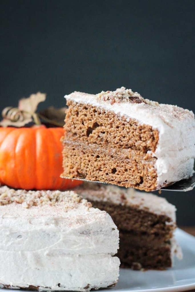 a slice of vegan pumpkin cake on a cake lifter with a pumpkin in the background