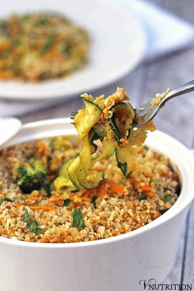 a fork picking up some vegetables out of a casserole dish with another plate of pumpkin casserole in the background