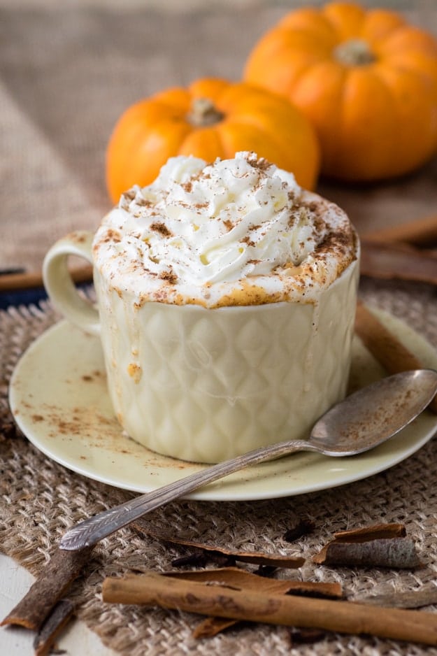 a mug of hot pumpkin spiced milk with two little pumpkins in the background 