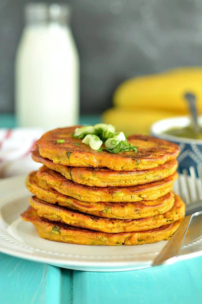 a stack of savory pumpkin pancakes on a white plate with green onions on the top and a bottle of milk in the background