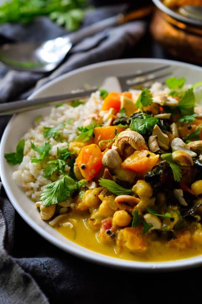 vegan pumpkin curry in a white bowl with a fork and cilantro in the background