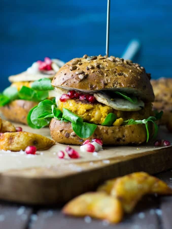 a vegan pumpkin burger on a wooden board with fries on the side and a blue background