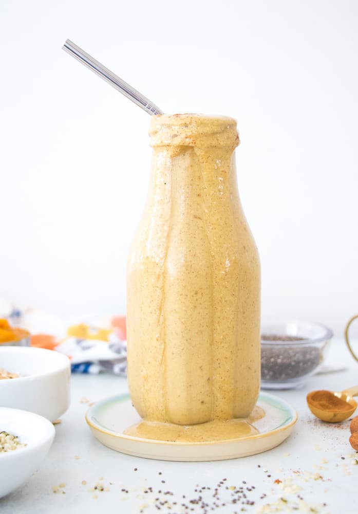 pumpkin protein smoothie in a glass bottle with a straw and a white background 