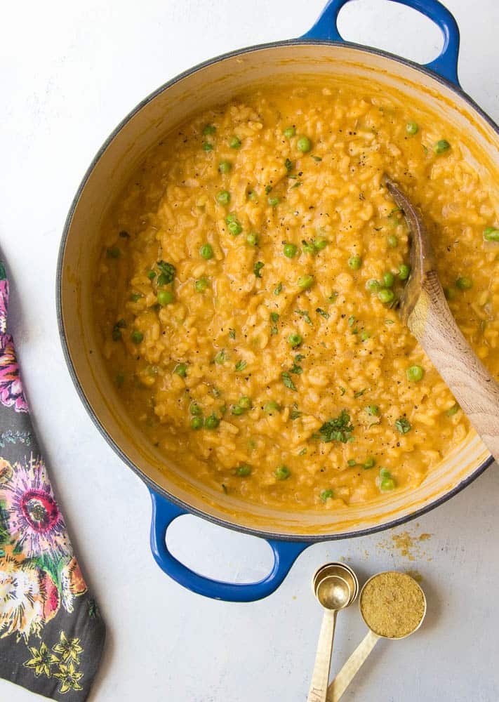 pumpkin risotto in a blue pot with a wooden spoon and a flower napkin on the side