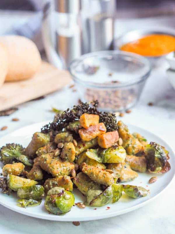 pumpkin gnocchi with Brussels sprouts on a white plate with a small bowl of sunflower seeds and bread in the background