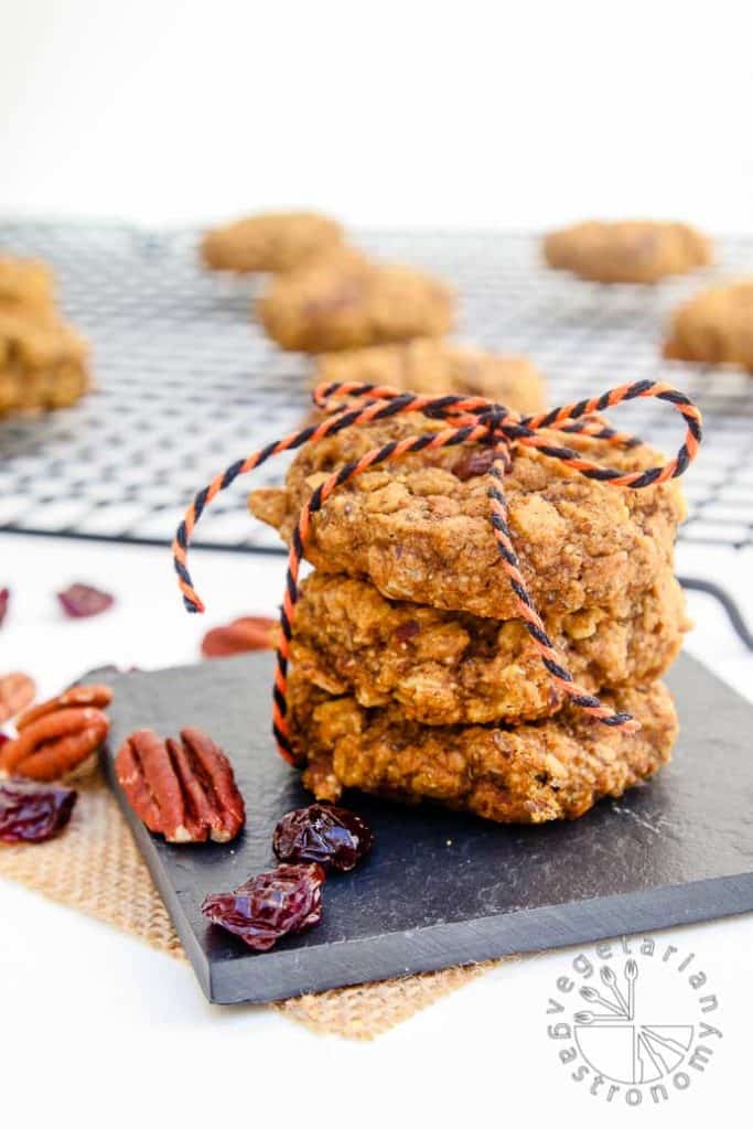 a stack of vegan pumpkin cookies with more cookies on a cooling rack in the background