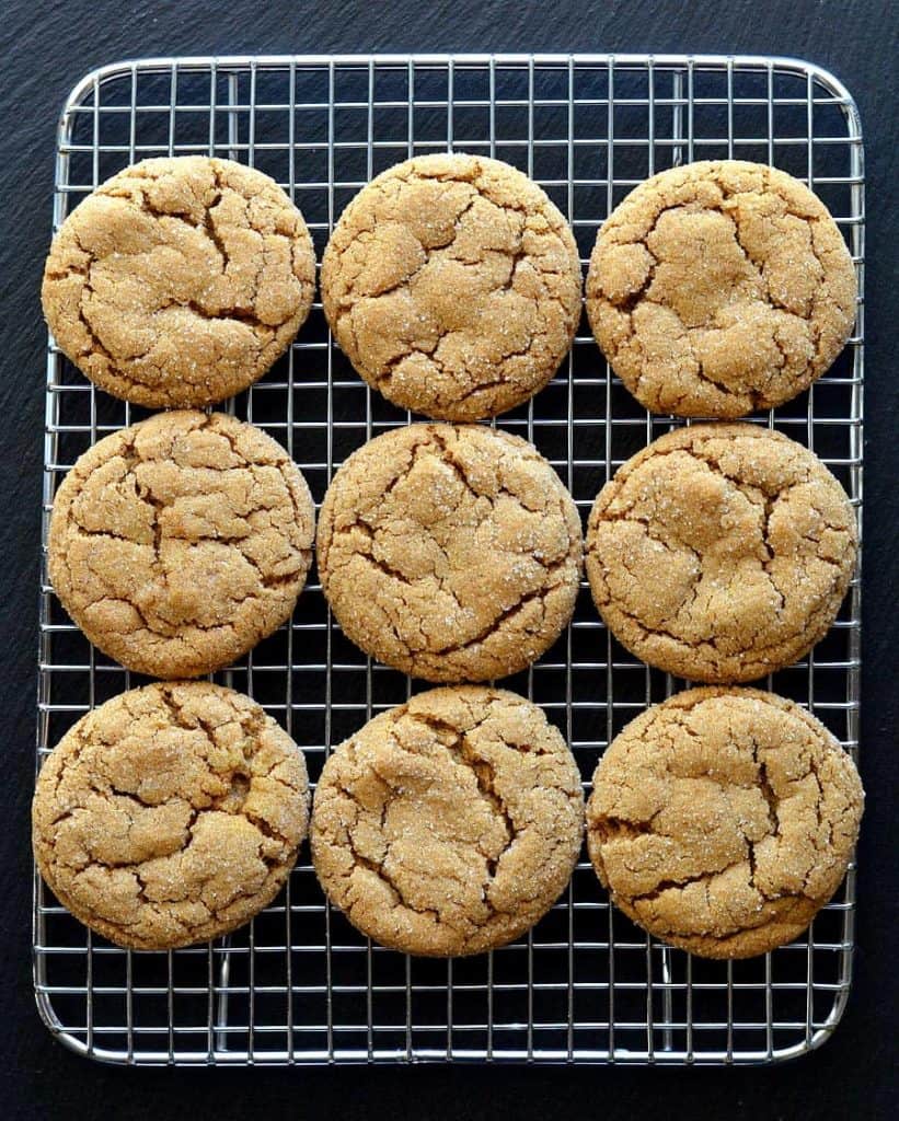 nine vegan pumpkin cookies on a cooling rack on a black surface