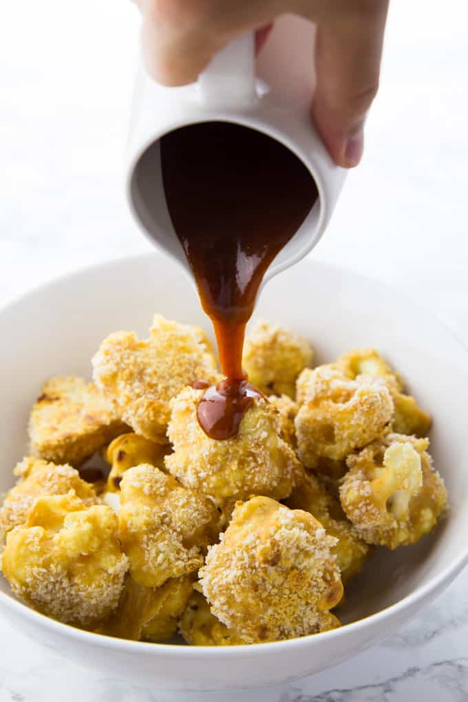 BBQ sauce is being poured over baked cauliflower wings in a bowl