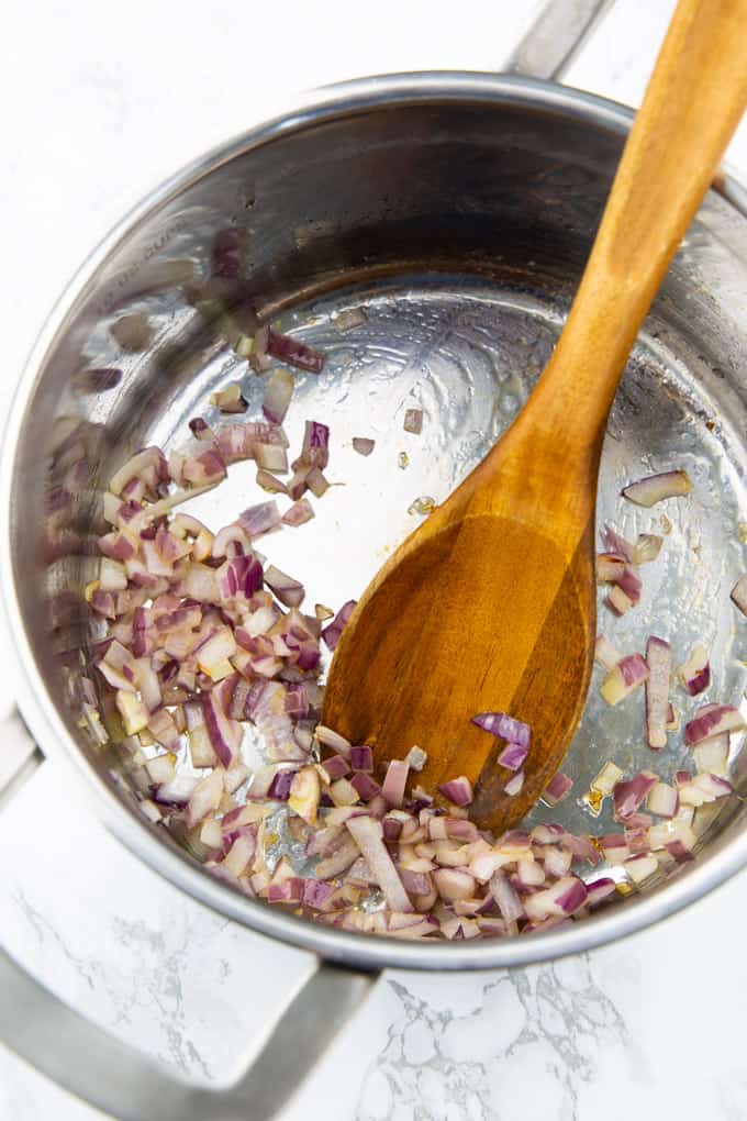 sautéed chopped red onion in a silver pot with a wooden spoon on a marble countertop 
