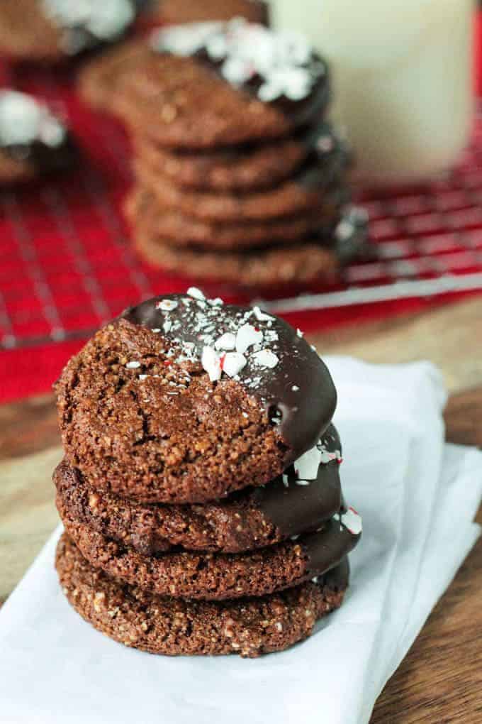 a stack of vegan chocolate gingerbread cookies on white parchment paper with more cookies and a glass of milk in the background
