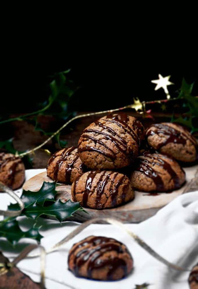 vegan lebkuchen drizzled with chocolate on a white dish cloth with Christmas decoration on the side and a black background