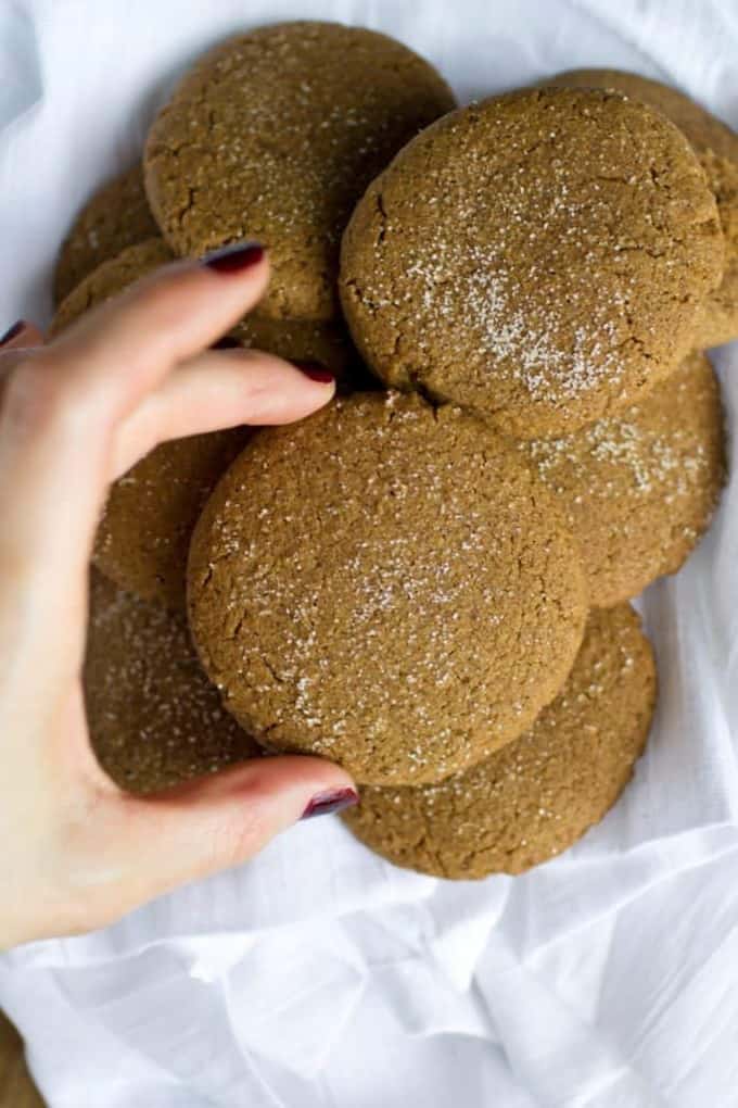 a hand holding a vegan ginger snap cookie over more cookies on a white dish cloth