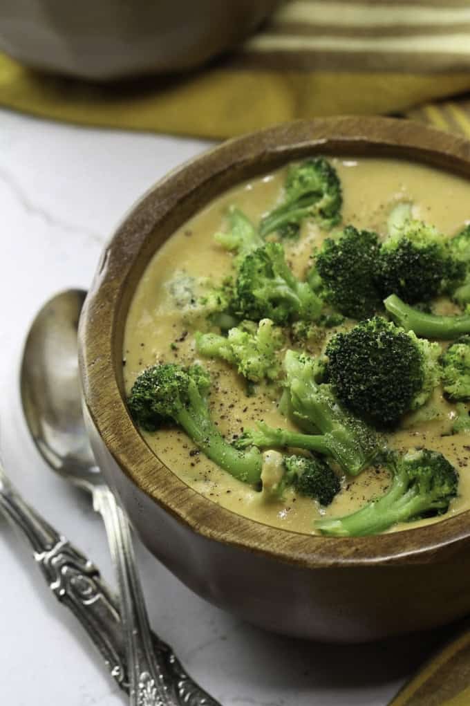 vegan sweet potato broccoli soup in a wooden bowl with cooked broccoli on top and a spoon on the side 