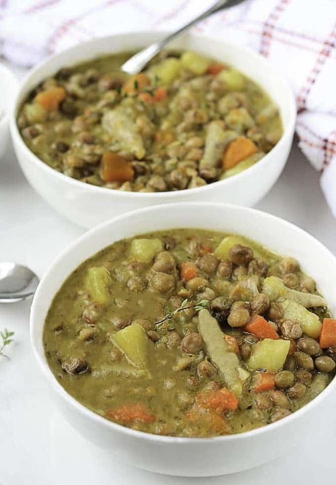 two white bowls of Jamaican pea soup on a white surface with a red and white dish cloth in the background 