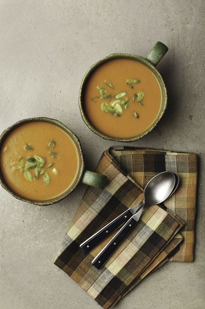 two bowls of pumpkin curry soup with green onions on top and a napkin and two spoons on the side 