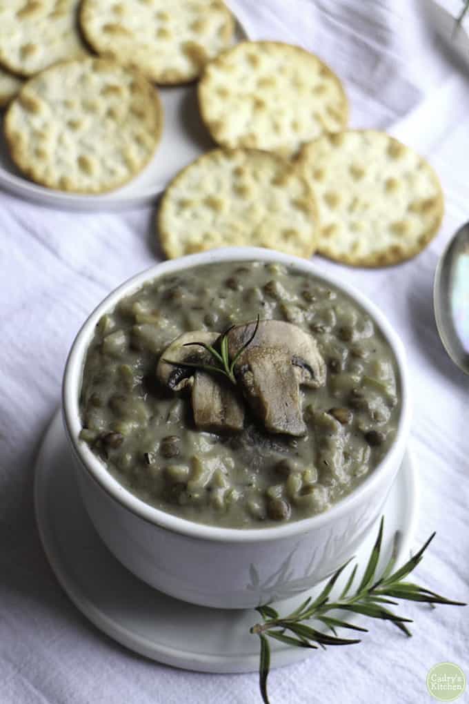 vegan mushroom rice soup in a white bowl with fresh rosemary and crackers in the background