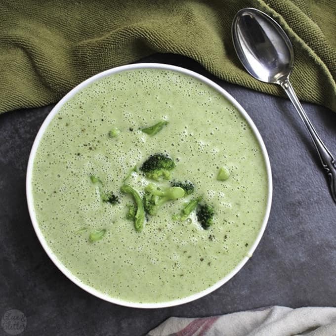 vegan broccoli soup in a white bowl on a grey and a green dish cloth with a spoon on the side 