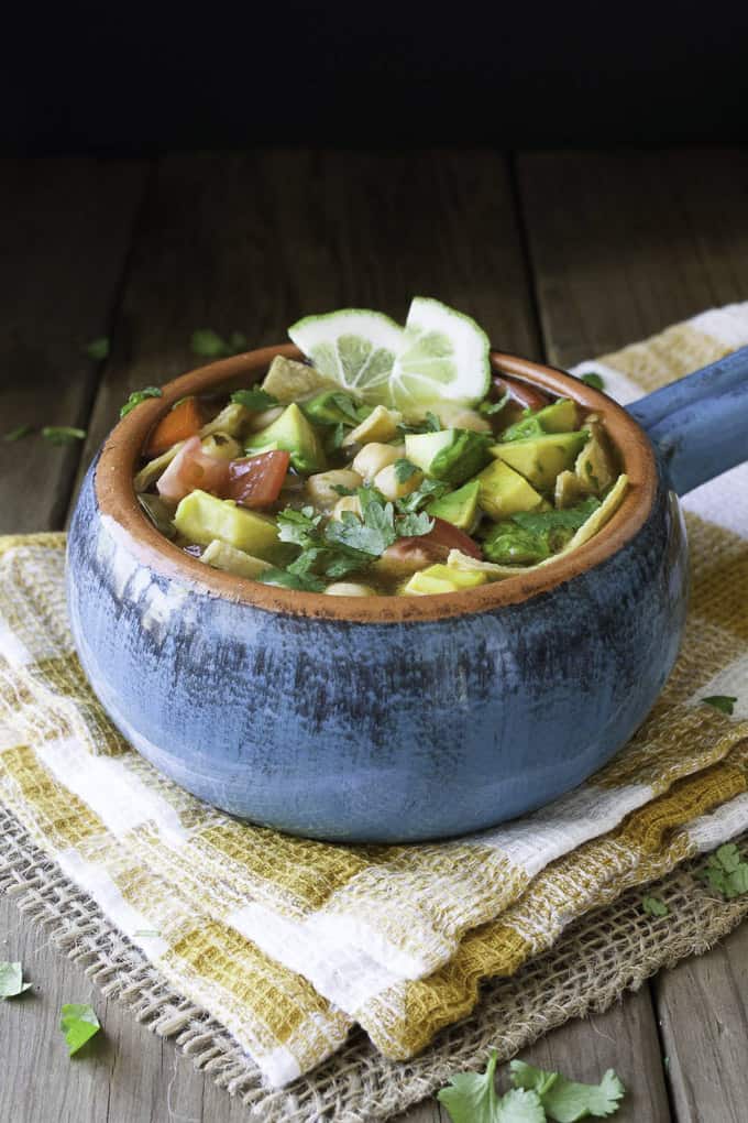 Mexican lime soup in a blue bowl with limes on top and fresh herbs on the side