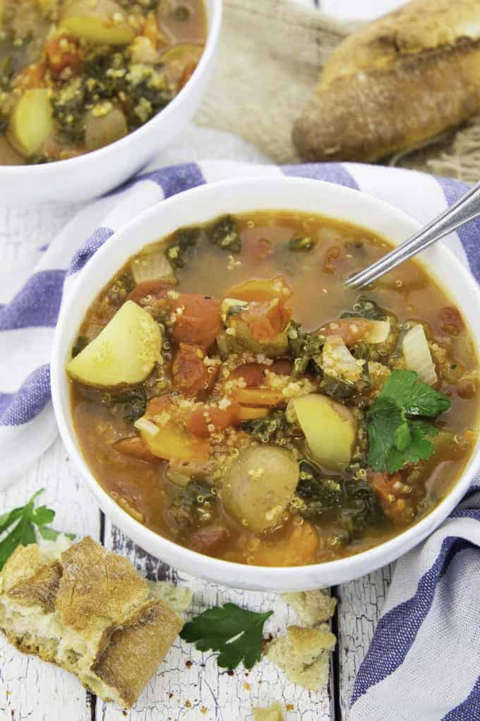 a bowl of quinoa soup on a white wooden board with some bread and fresh herbs on the side 