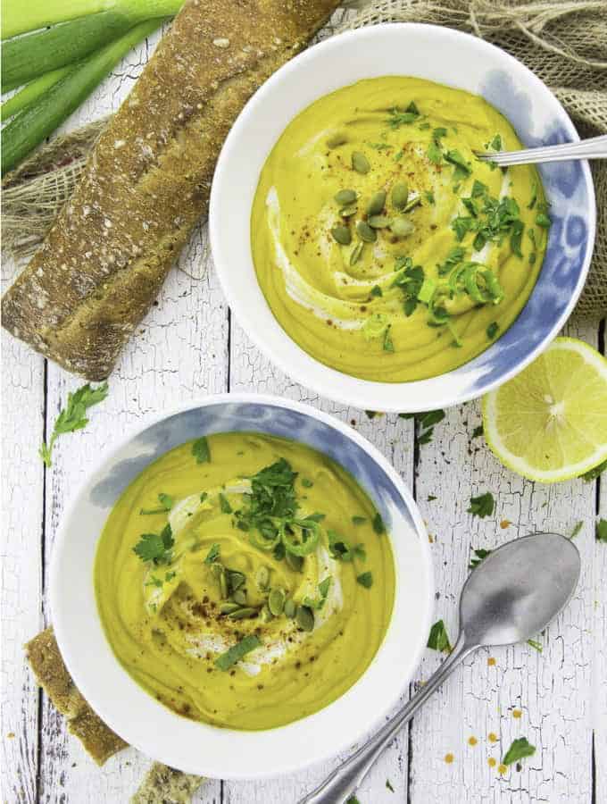 two bowls of vegan red lentil soup on a white wooden board with bread, a spoon, and a lemon on the side 