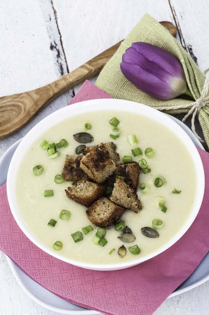 vegan potato leek soup on a white wooden board with a pink napkin and a wooden spoon