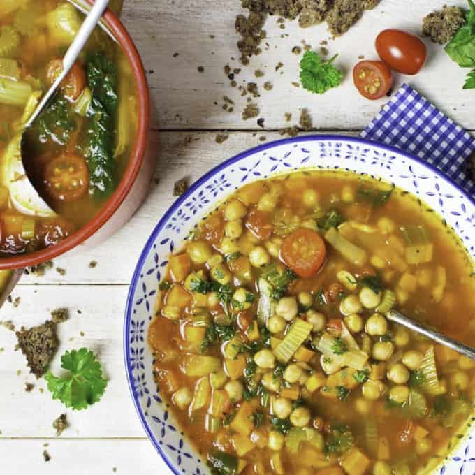 vegan chickpea soup in a blue and white bowl with a pot of soup and bread on the side 