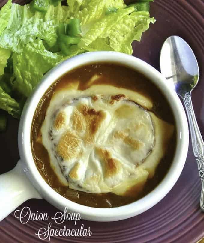 vegan French onion soup in a white bowl with lettuce in the background and a spoon on the side 