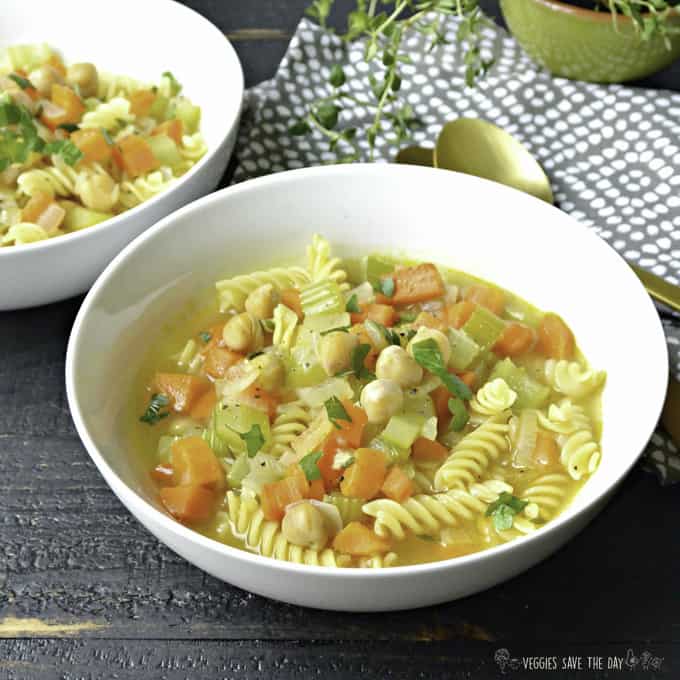 vegan chickpea noodle soup in a white bowl on a dark wooden surface with a spoon and another bowl of soup in the background