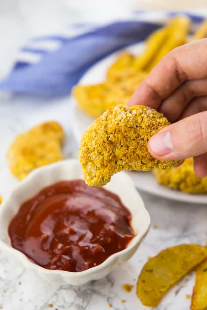 A Hand Holding a Vegan Chicken Nugget with a Bowl of Ketchup and Fries on the Side 