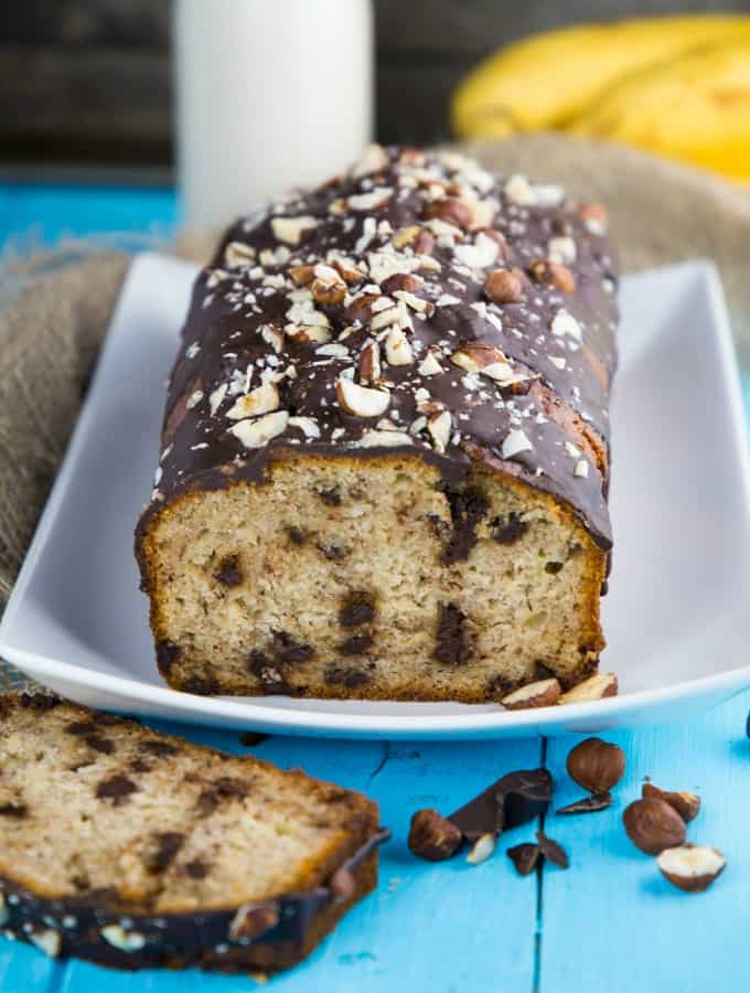 a chocolate-covered vegan banana bread on a white plate on a blue wooden board