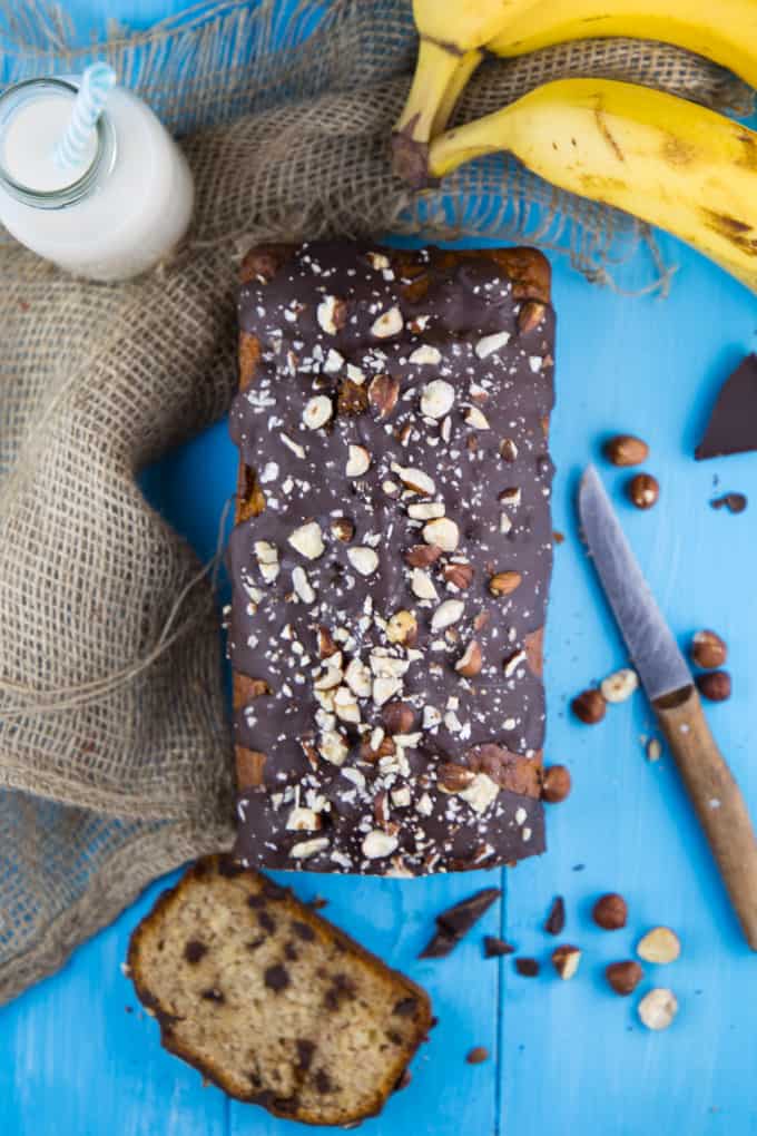 a banana bread on a blue wooden board with bananas and hazelnuts on the side